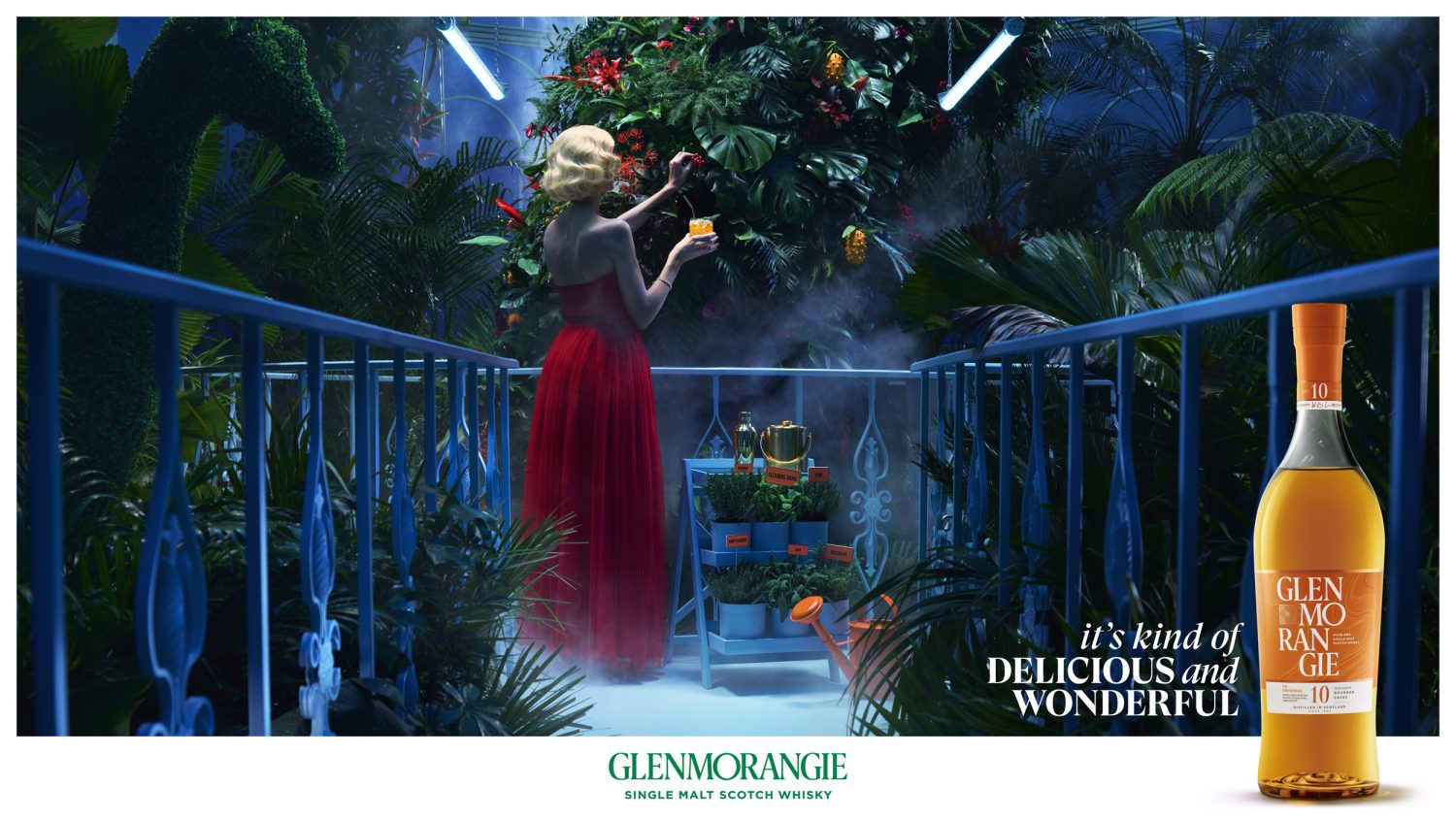 Glenmorangie ad shows a woman in a red dress tending to plants in a blue garden with a bottle of scotch on a white backdrop.
