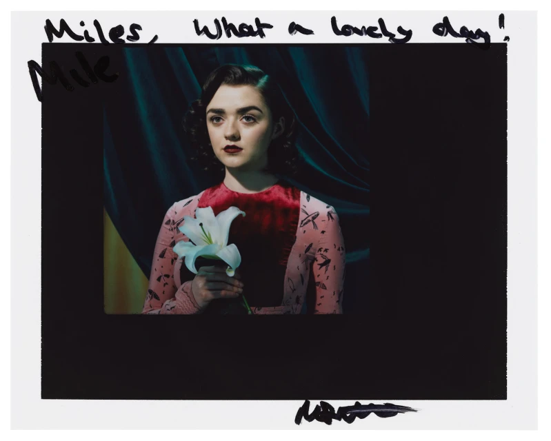 Glamorous portrait of a young woman with red lips, holding a white lily in front of a dark teal and yellow backdrop with handwritten text.