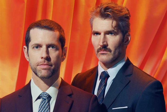 Two adult males, one with a mustache and grey hair, posing in suits against an orange backdrop for a formal studio portrait.