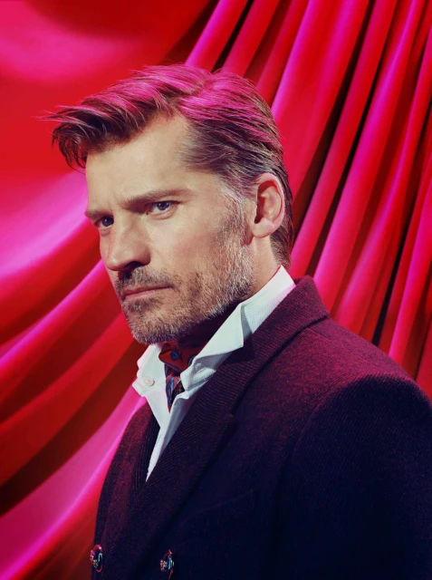 Portrait of adult male with graying hair wearing a dark double-breasted coat and patterned neckwear against a pink-red draped backdrop.