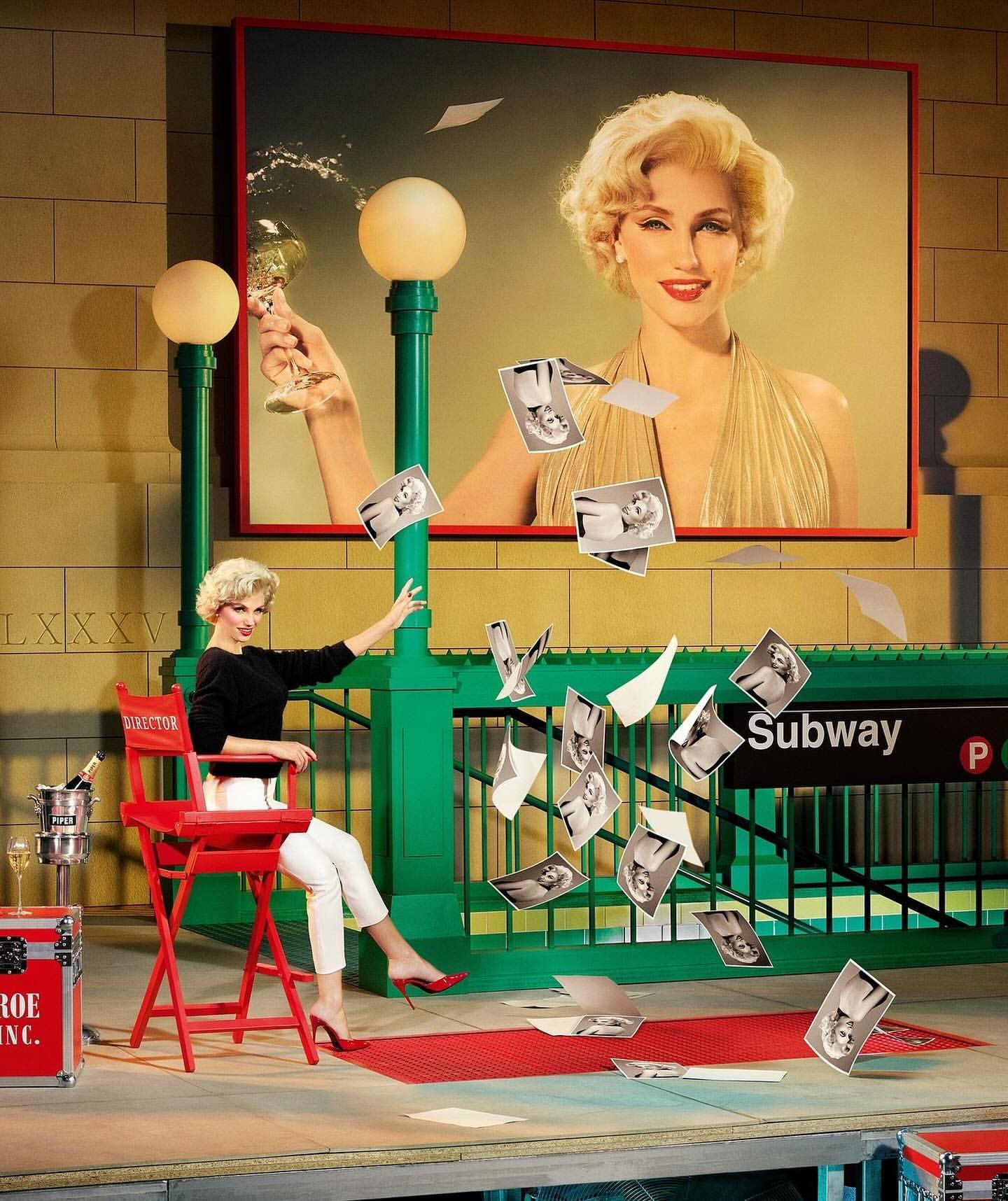 Woman in Marilyn Monroe style poses near subway entrance with falling photos and billboard featuring a model in a gold dress.