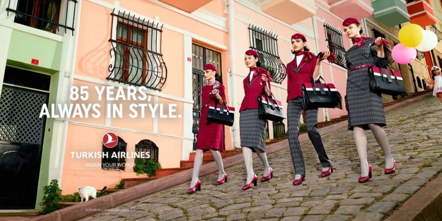 Turkish Airlines ad features four female flight attendants in uniform walking on a cobblestone street, holding handbags and balloons.