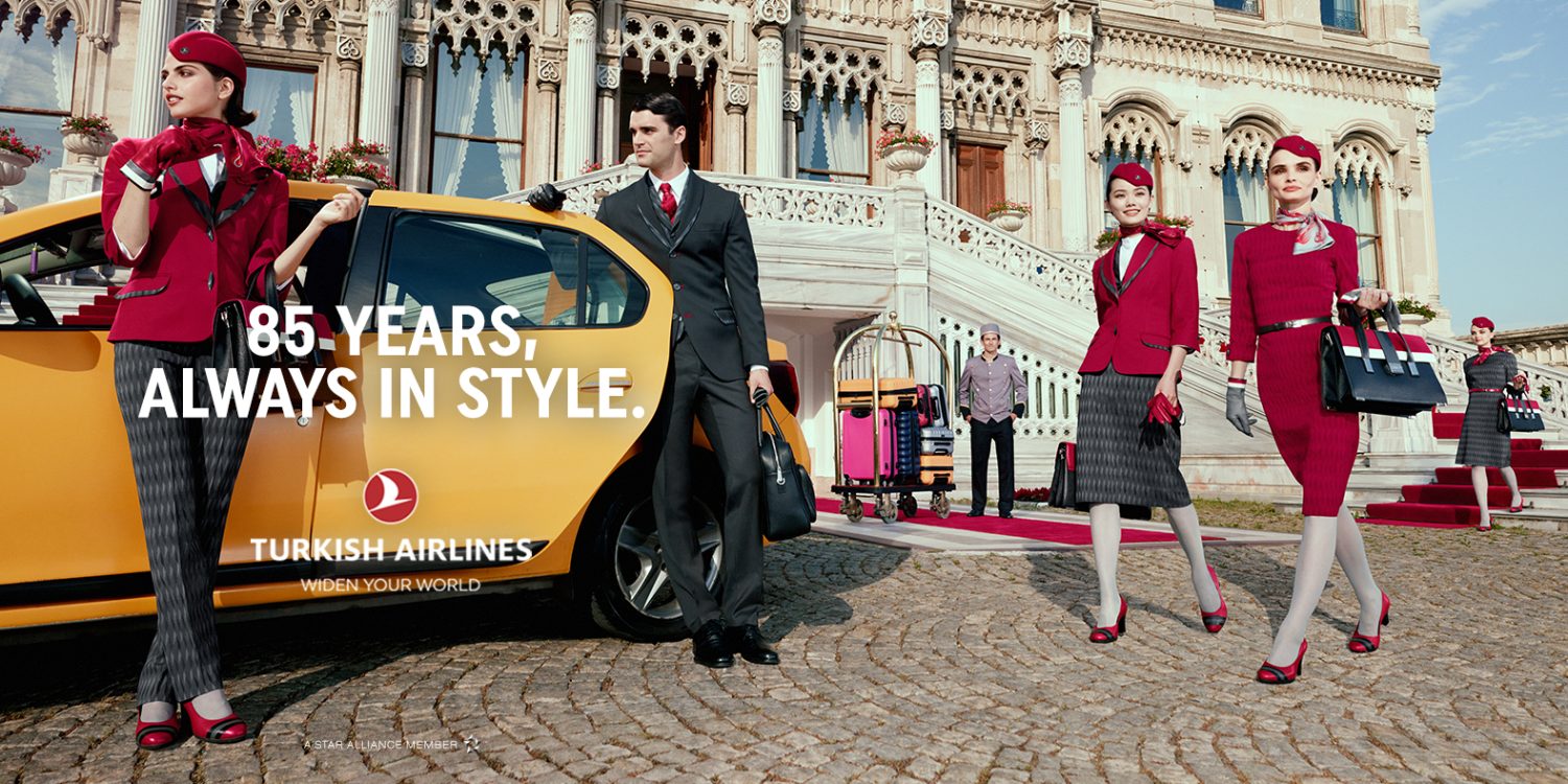 Turkish Airlines advertisement featuring flight attendants in red uniforms and a businessman standing near a yellow taxi against ornate architecture.