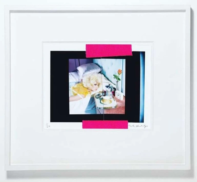 Framed artwork of woman in bed, breakfast tray, and rose, photo with pink tape overlay on white background, bedroom setting, indoor.