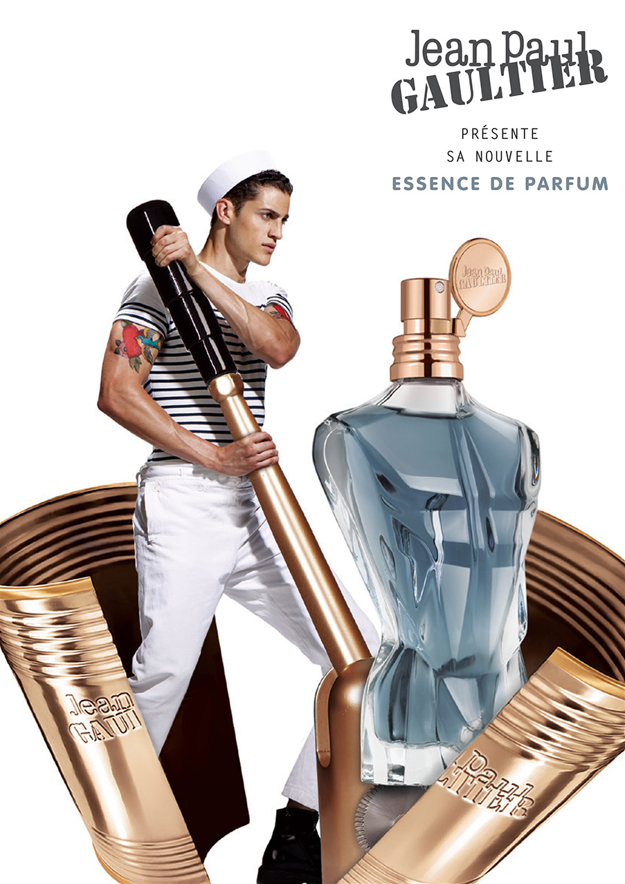 Jean Paul Gaultier fragrance advertisement features male model in sailor hat, perfume bottle, and product tubes on a white backdrop.