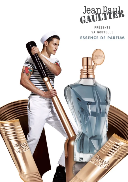 Jean Paul Gaultier fragrance advertisement features male model in sailor hat, perfume bottle, and product tubes on a white backdrop.