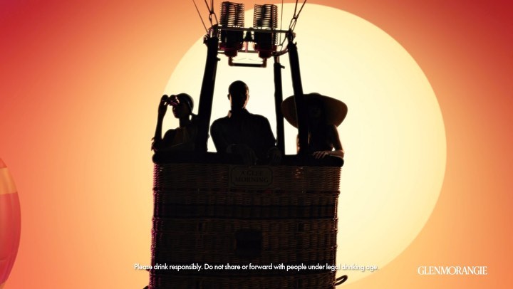 Silhouette of three people inside a hot air balloon against a radiant sunset, promoting responsible drinking of Glenmorangie.