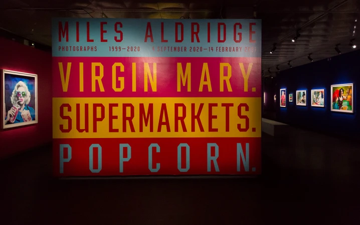 Artwork in gallery featuring a vibrant sign with text and art pieces on the wall, illuminated by gallery lighting in a museum space.