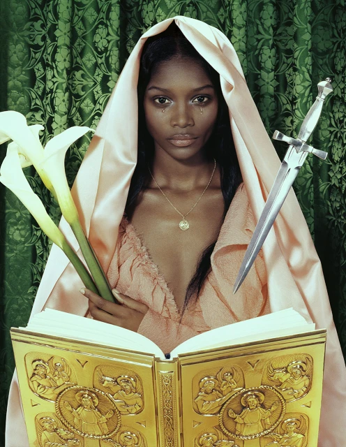 A woman with dark skin and tears is wearing a draped robe and holding lilies and a dagger in front of a gold book.