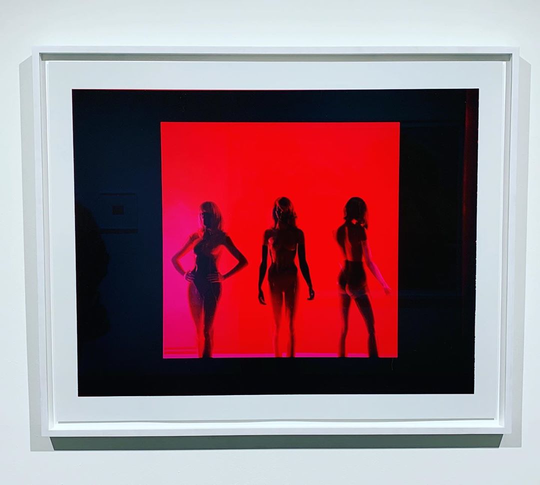 Framed art photograph features silhouettes of three figures against a vibrant red background, creating a striking and artistic composition.