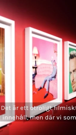 Three framed photographs hang on a red wall, displaying a man in a pink room, a portrait, and a warm-toned image.