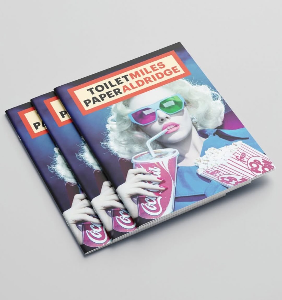 Close-up of three fashion magazines stacked, featuring a woman with retro 3D glasses drinking Coca-Cola and eating popcorn.