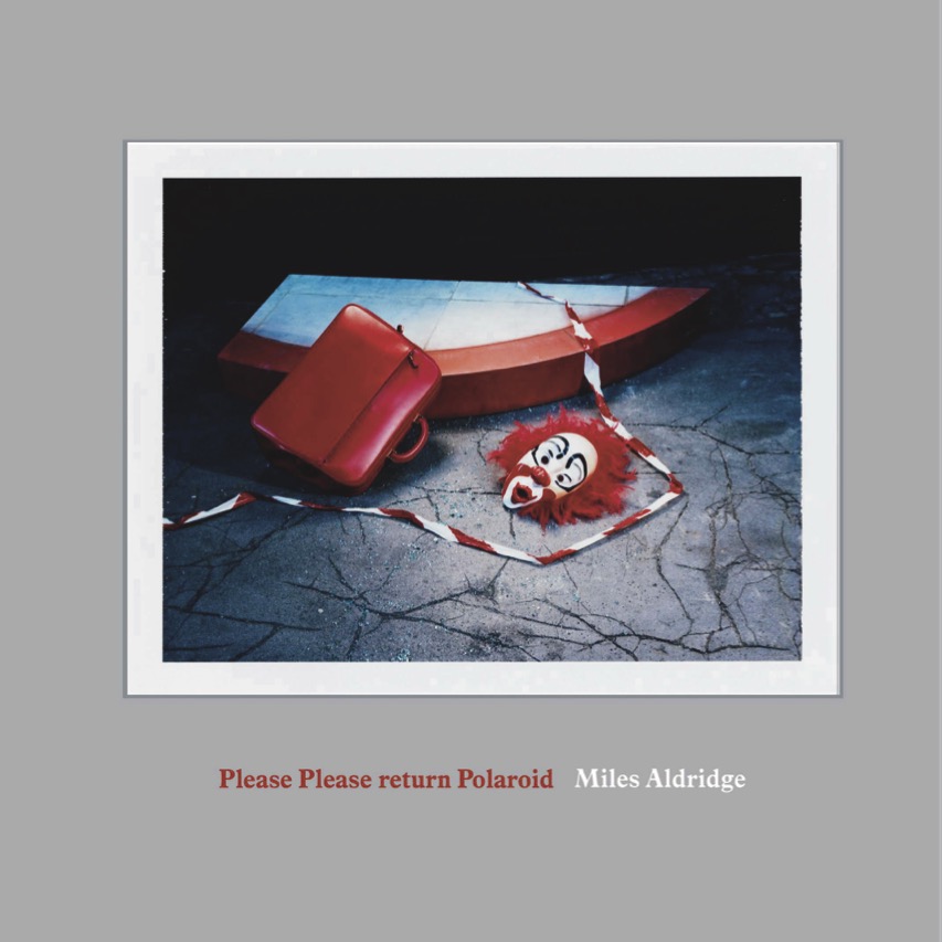 Striking still life with a red briefcase, a fragmented boat, and a clown mask, set against a cracked floor and dark backdrop.