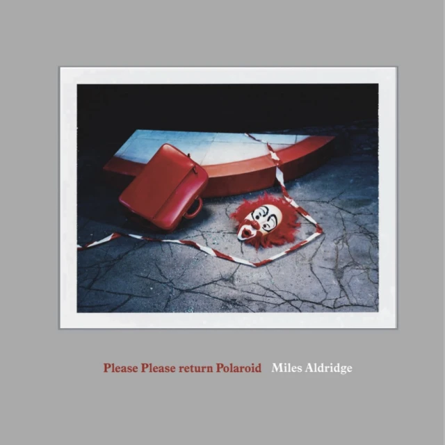 Striking still life with a red briefcase, a fragmented boat, and a clown mask, set against a cracked floor and dark backdrop. 