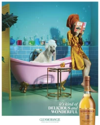 Woman in satin robe and orange hair wrap reading a book in a bathroom with a dog in a pink bathtub, photographed by Miles Aldridge