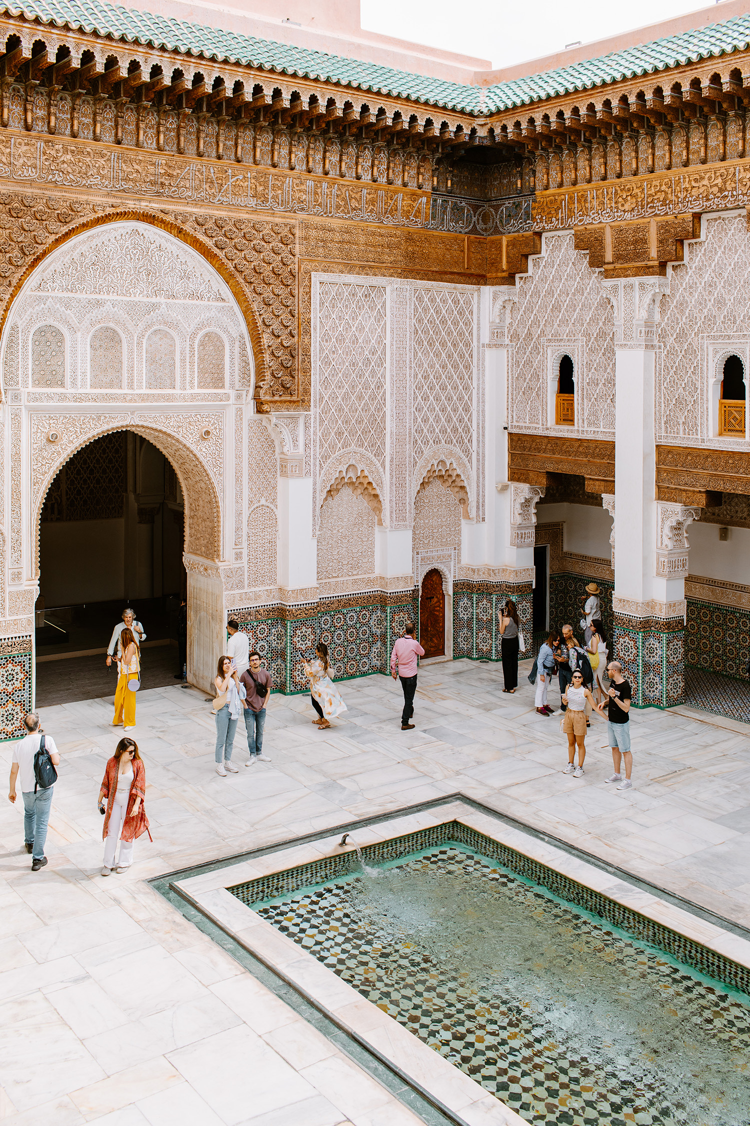 Courtyard view of the Ben Youssef Madrasa in Marrakesh, Morocco featuring a rectangular fountain and many tourists visiting the historic site.