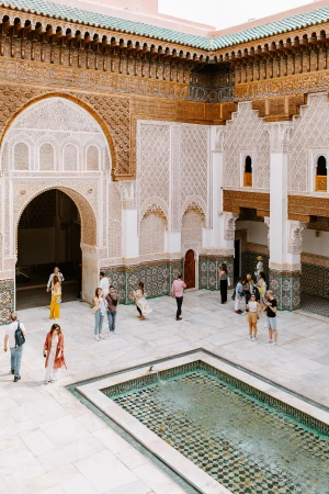 Courtyard view of the Ben Youssef Madrasa in Marrakesh, Morocco featuring a rectangular fountain and many tourists visiting the historic site.