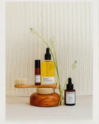 Perenae skincare bottles with yellow facial oil and amber glass droppers arranged with a wooden brush on a textured backdrop.
