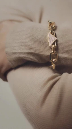 Close-up of a gold chain-link bracelet with a triangle charm accent adorning a person's wrist, set against a neutral sweater background.
