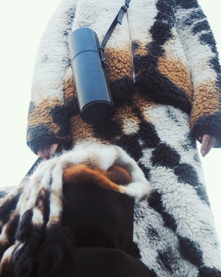 Person in patterned faux fur coat with water bottle on strap. Warm tones and soft texture, winter fashion, outdoor shot.