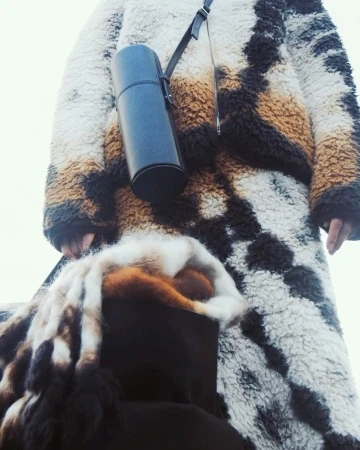 Person in patterned faux fur coat with water bottle on strap. Warm tones and soft texture, winter fashion, outdoor shot.