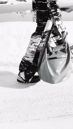 Monochrome fashion photograph showing patterned trousers and a large slouchy shoulder bag outdoors in snow
