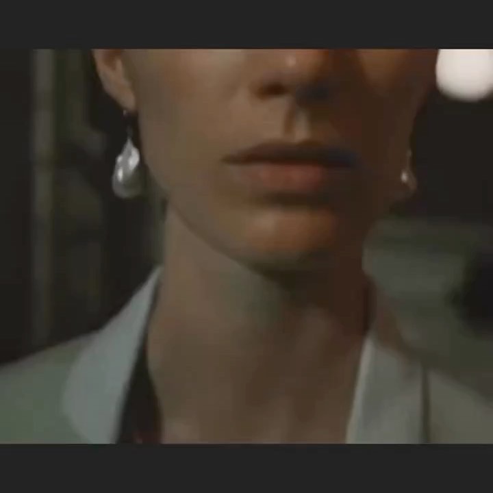 Close-up view of an adult female wearing teardrop earrings and a white jacket, showing her neckline and facial features.