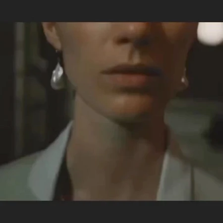 Close-up view of an adult female wearing teardrop earrings and a white jacket, showing her neckline and facial features.