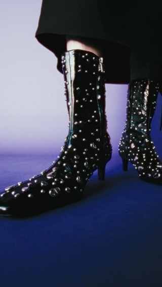 Fashionable black patent leather studded boots with block heels displayed against a background gradient of blue and lavender.