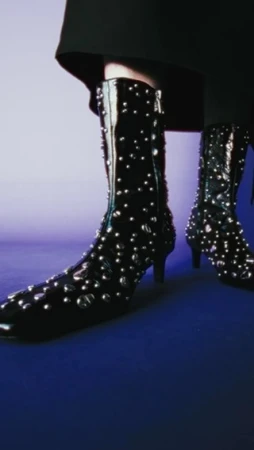 Fashionable black patent leather studded boots with block heels displayed against a background gradient of blue and lavender.