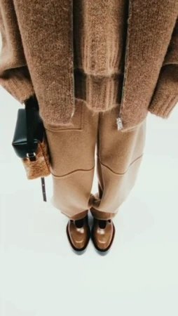 Person wearing a brown fuzzy sweater, matching pants, and dark T-strap shoes, accessorized with a structured black and tan purse.