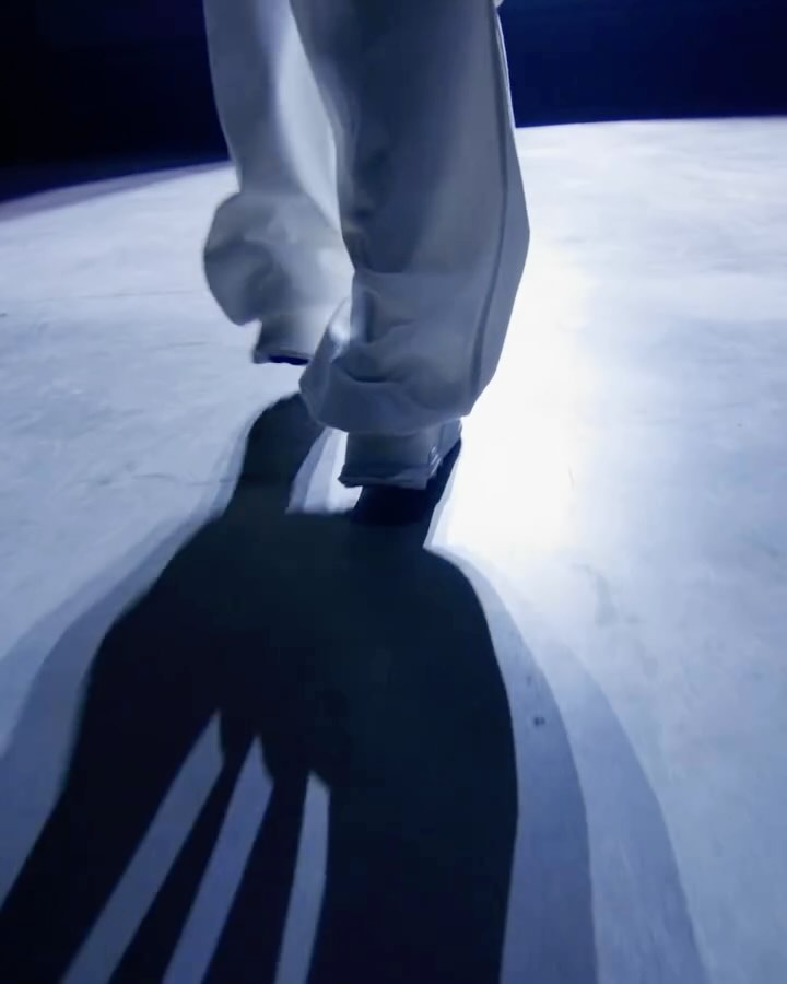 Low angle shot of a person wearing white trousers walking forward, casting a long dark shadow on the floor.