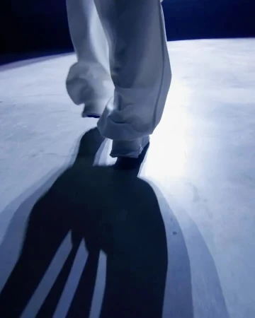 Low angle shot of a person wearing white trousers walking forward, casting a long dark shadow on the floor.