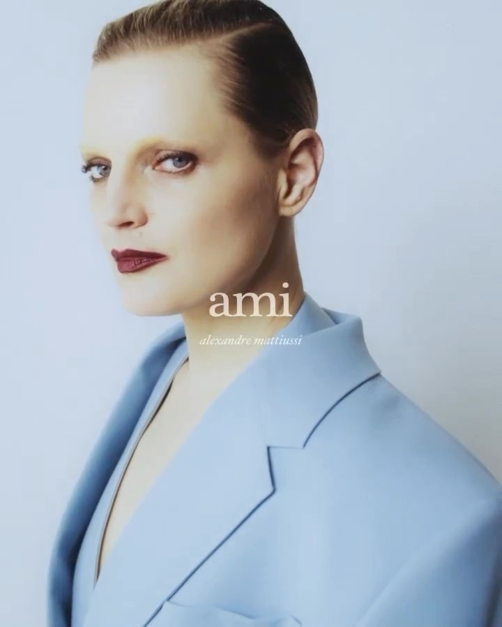 Close-up fashion shot of a woman with light skin and dark lipstick wearing a blue blazer, posing against a light background.