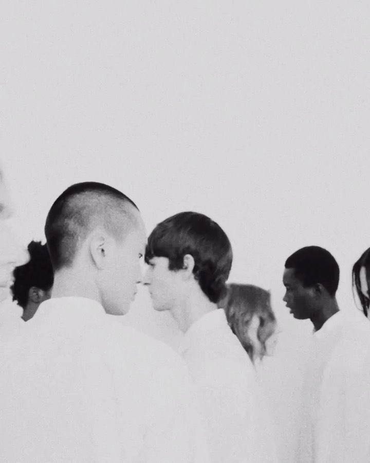 Monochromatic shot of diverse people standing closely in white shirts, creating a minimalist and uniform aesthetic against a light backdrop.