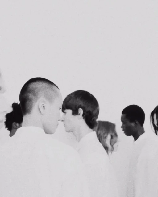 Monochromatic shot of diverse people standing closely in white shirts, creating a minimalist and uniform aesthetic against a light backdrop.