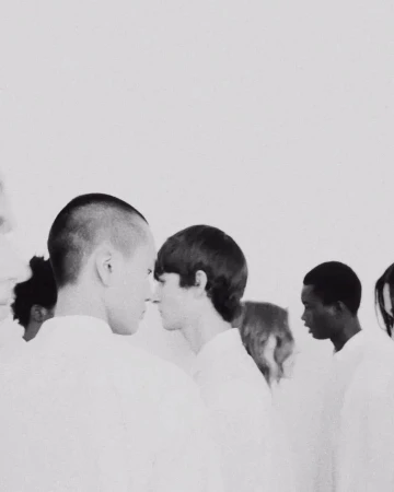 Monochromatic shot of diverse people standing closely in white shirts, creating a minimalist and uniform aesthetic against a light backdrop.