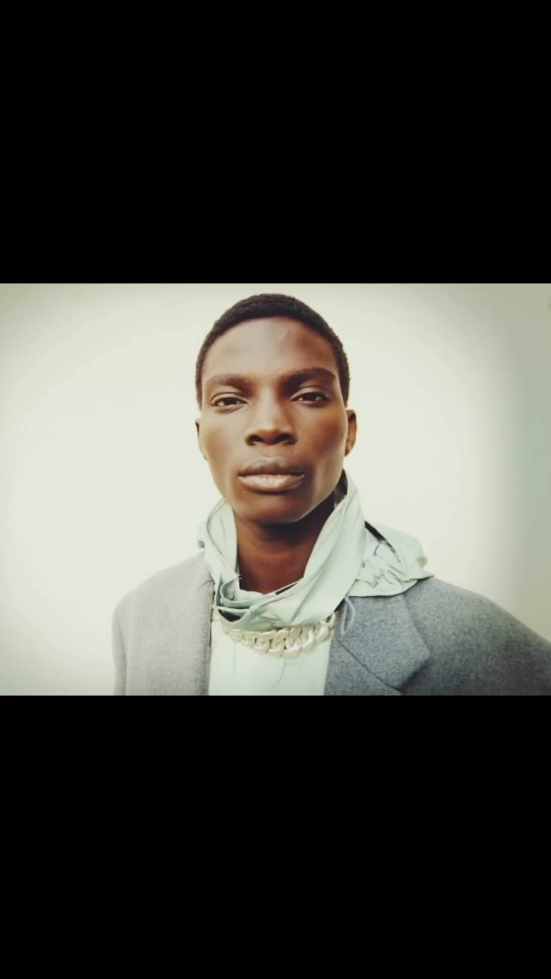 Headshot of an African-American male model in a gray coat and mint green hooded top, looking directly at the camera with a neutral expression.