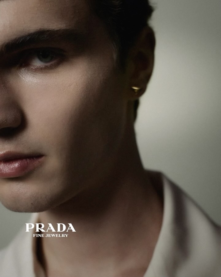 Close-up studio shot of a fair-skinned young adult male wearing a gold earring and a white collared shirt. Fashion advertisement.