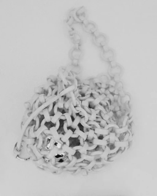 Close-up of a white, woven, bucket-style handbag with a chain handle against a light background, emphasizing texture and craftsmanship.
