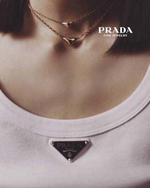 Close-up of a woman wearing layered gold necklaces and a white t-shirt with a Prada logo, showcasing fine jewelry.