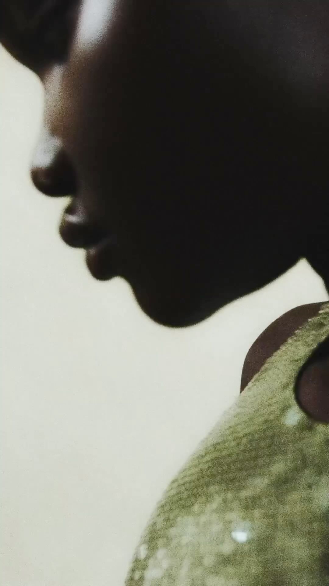 Close-up profile of a Black female adult with a sequined garment. Dark complexion, neutral expression, facing left against a neutral background.