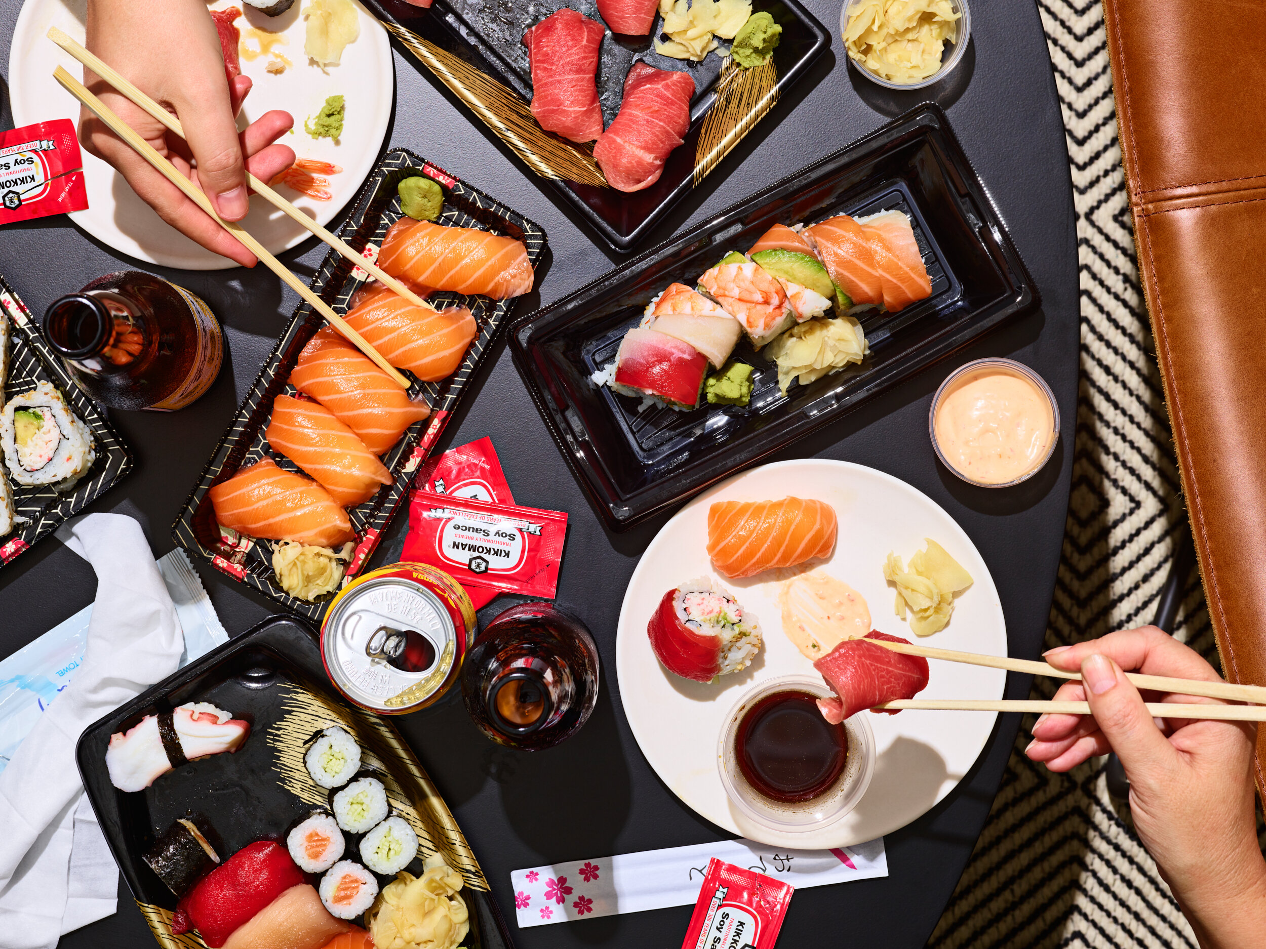 Overhead view of assorted sushi, including nigiri and rolls, on a black table with various dipping sauces, and drinks.