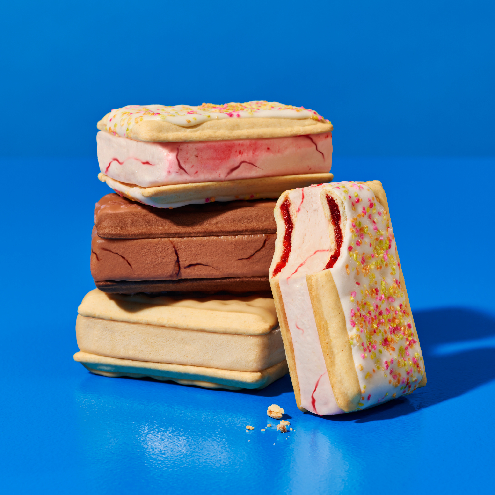 Stack of colorful ice cream sandwiches on a bright blue background with crumbs, dessert food photography, close-up angle, studio shot.