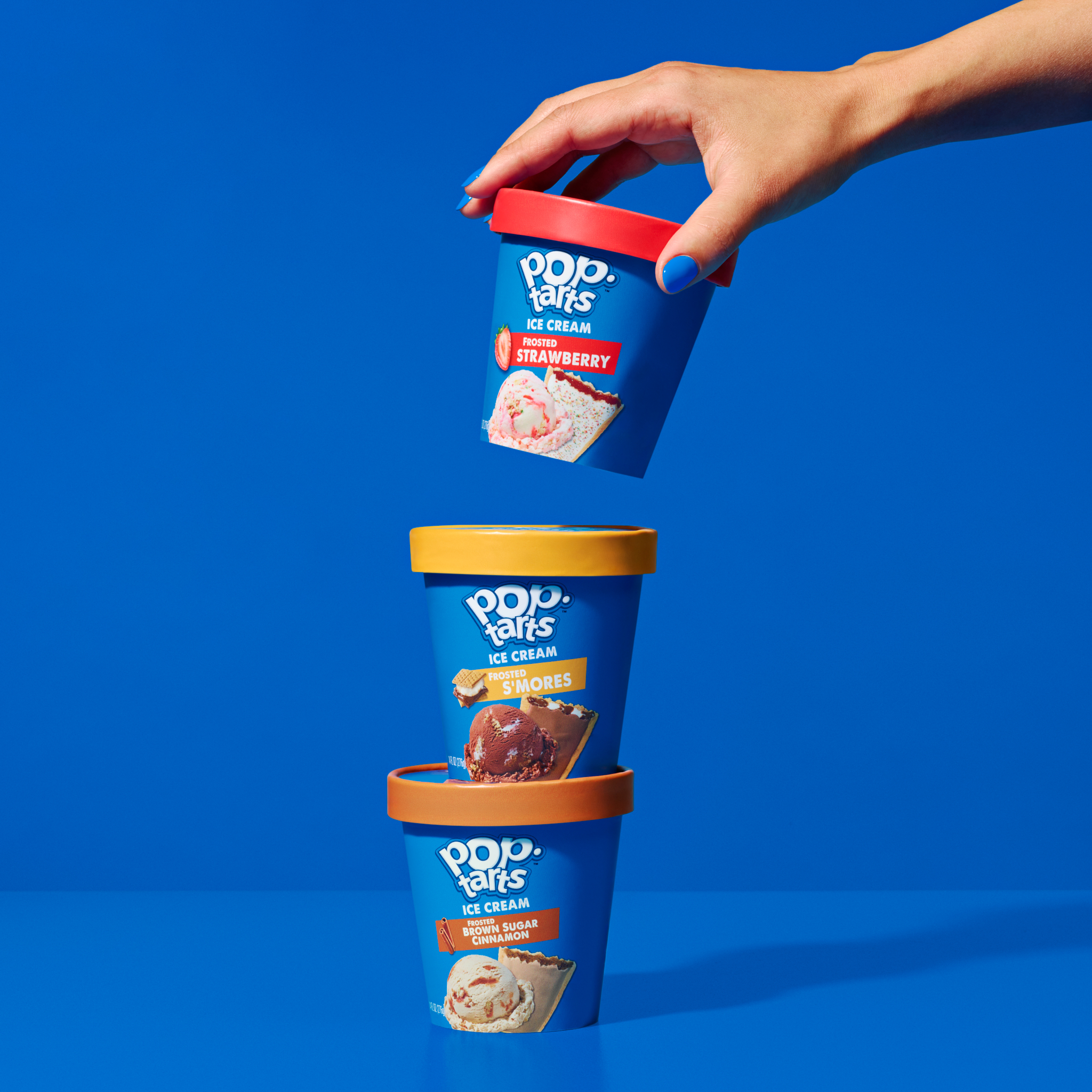 Three vibrant Pop-Tarts ice cream pints stacked against a bright blue backdrop, showcasing strawberry, s'mores, and brown sugar cinnamon flavors.