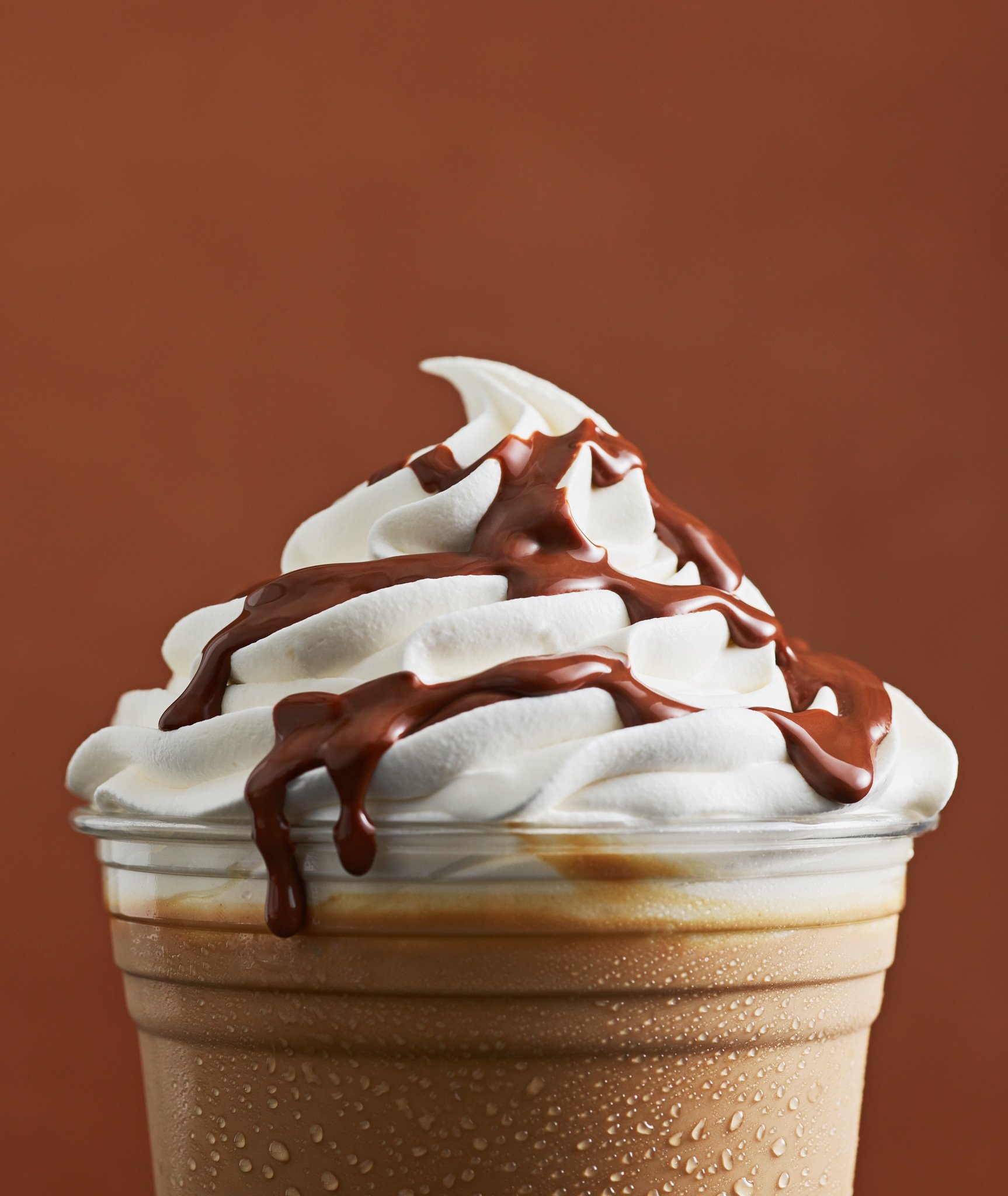 Close-up of a chocolate frappe with whipped cream on a brown background, highlighting its rich textures and colors.