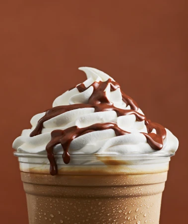 Close-up of a chocolate frappe with whipped cream on a brown background, highlighting its rich textures and colors.