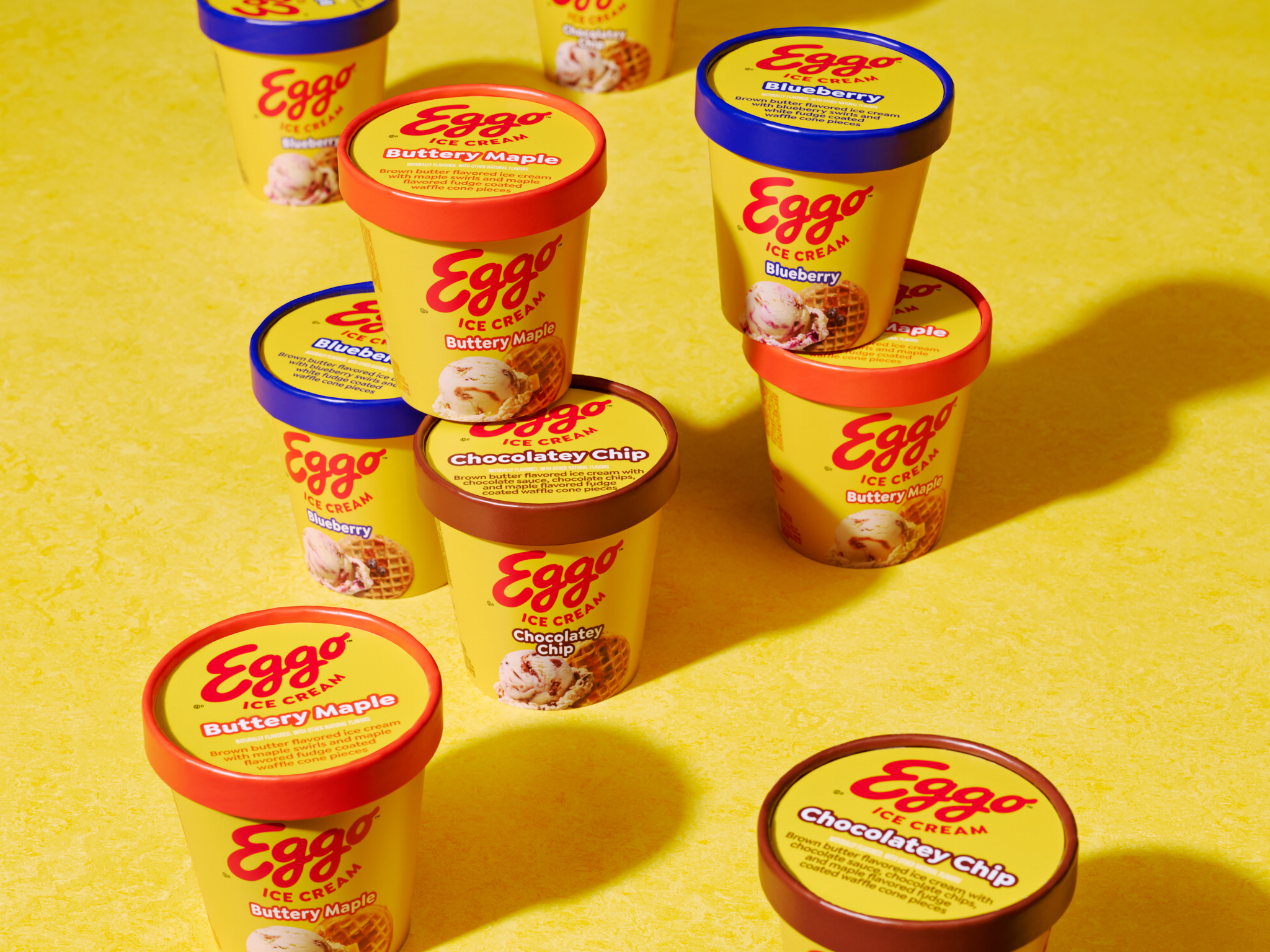 Eggo ice cream tubs featuring Buttery Maple, Blueberry, and Chocolatey Chip flavors, arranged on a bright yellow surface.