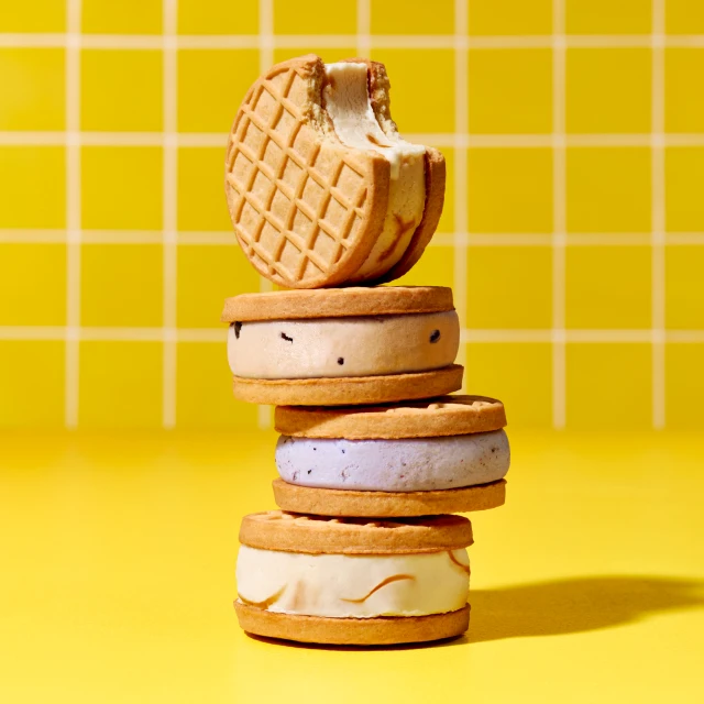 A stack of ice cream sandwiches with waffle cookies sits in front of a yellow grid background, creating a sweet and visually appealing dessert image.