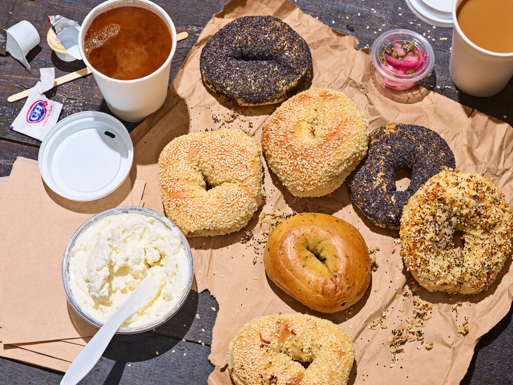 Overhead shot of assorted bagels with cream cheese and coffee on craft paper, creating a vibrant, appealing food still life.